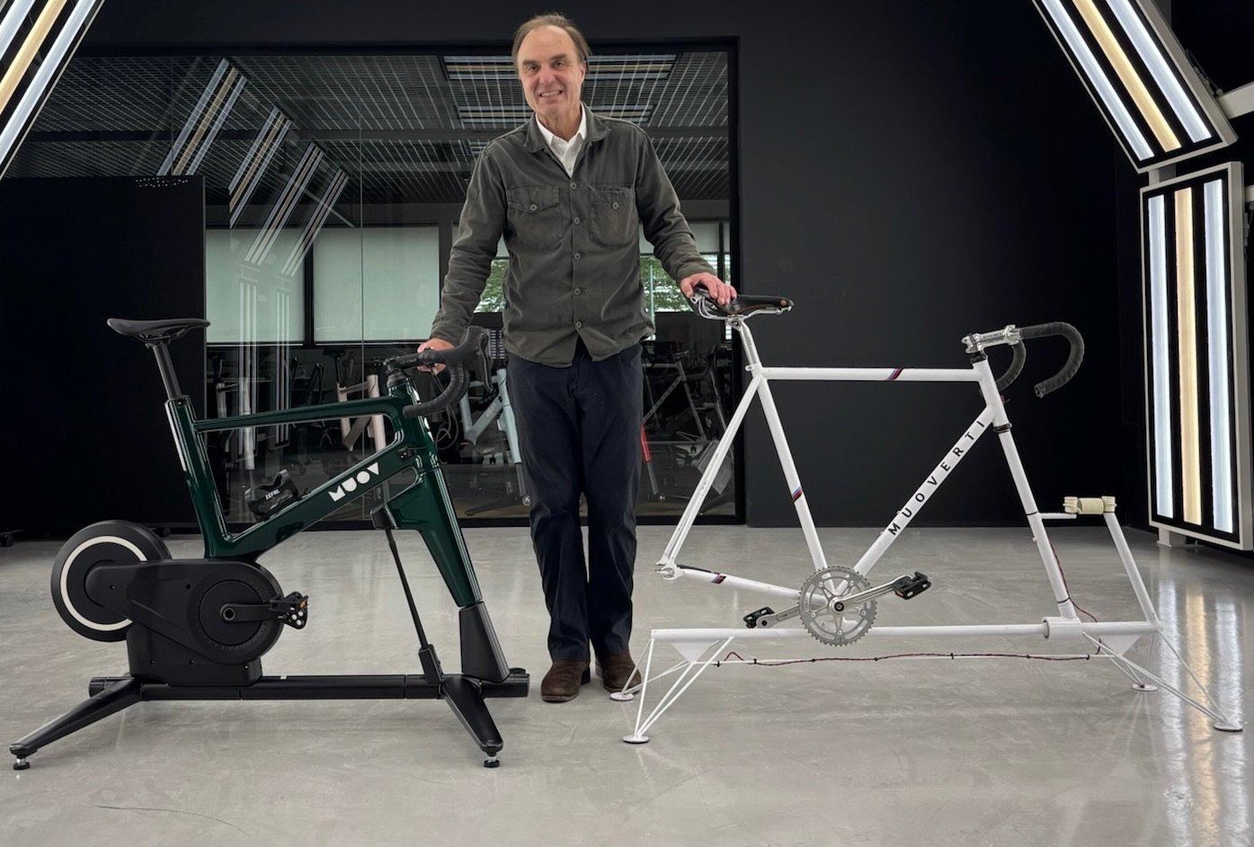 A man standing between a deep green MUOV bike and an early white MUOVERTI frame in a studio
