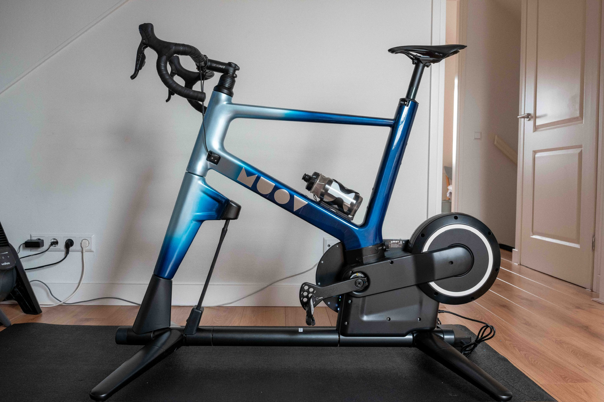 MUOV bike with a frame fading from deep blue into metallic silver, on a wooden floor in a home room