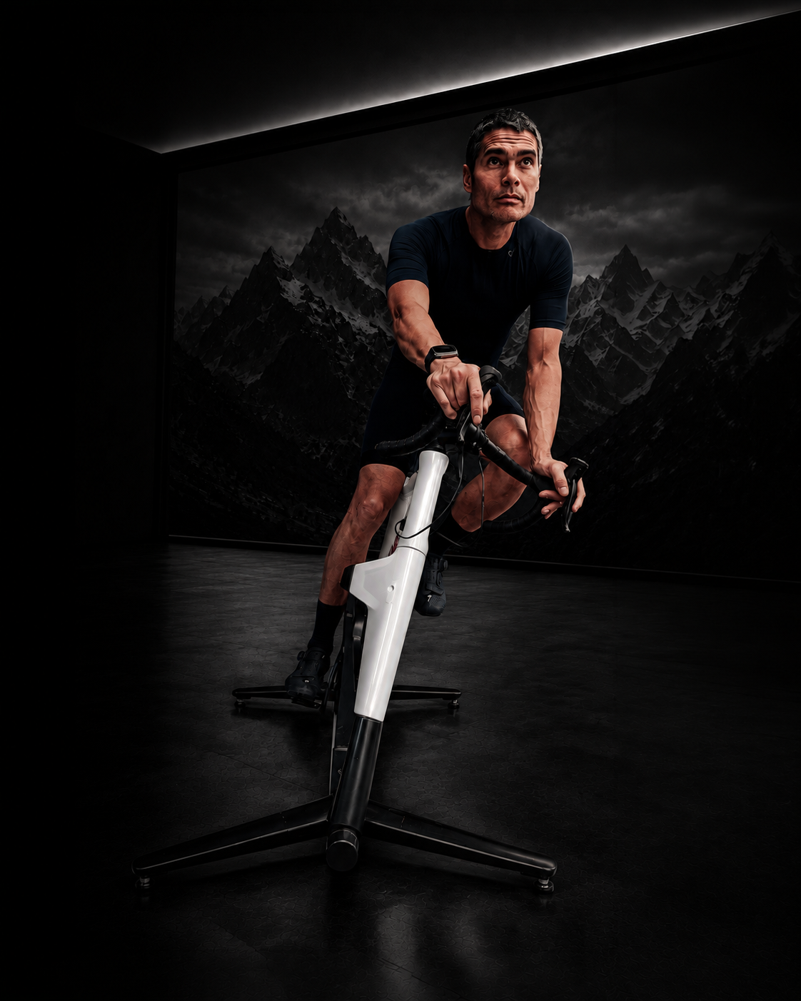 Rider leaning forward on a white MUOV bike in a dark studio, mountain landscape projected behind
