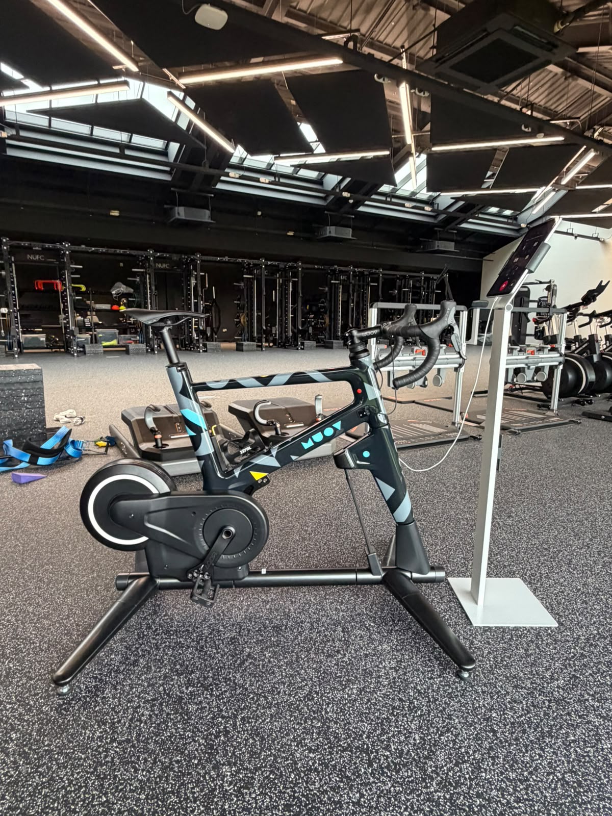 MUOV bike with a dark teal and grey camouflage painted frame, set up beside a screen in a performance gym
