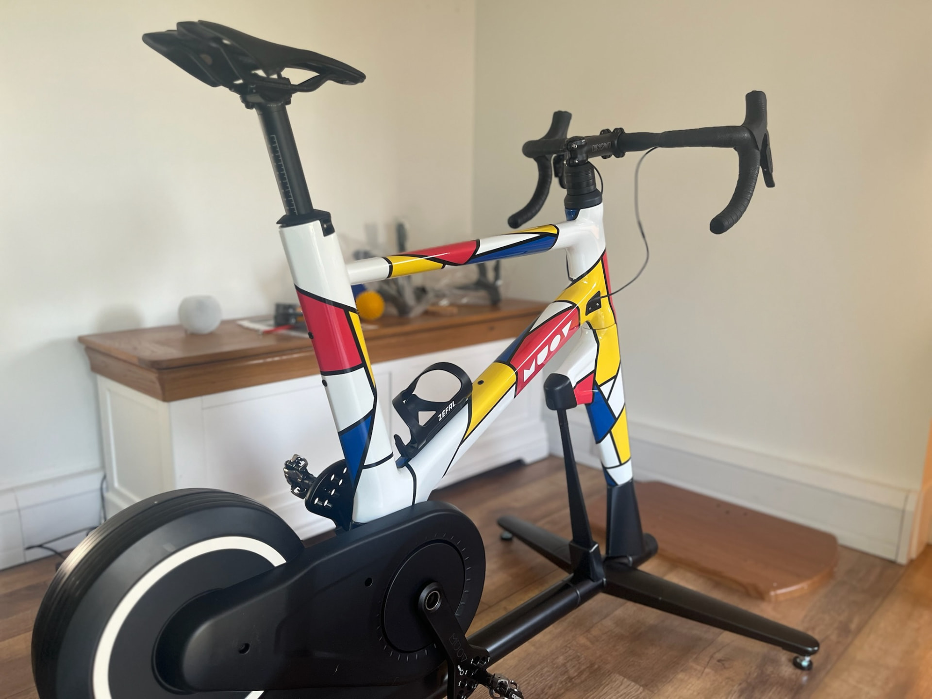 MUOV bike with a white frame painted in red, yellow and blue blocks outlined in black, in a living room