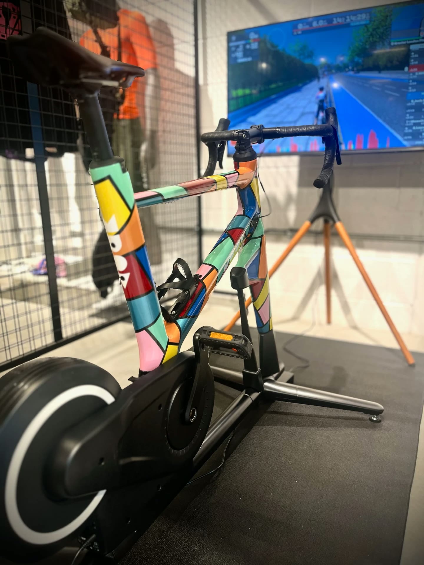 MUOV bike with a multicolour geometric painted frame in green, pink, yellow, blue and red, in a training studio